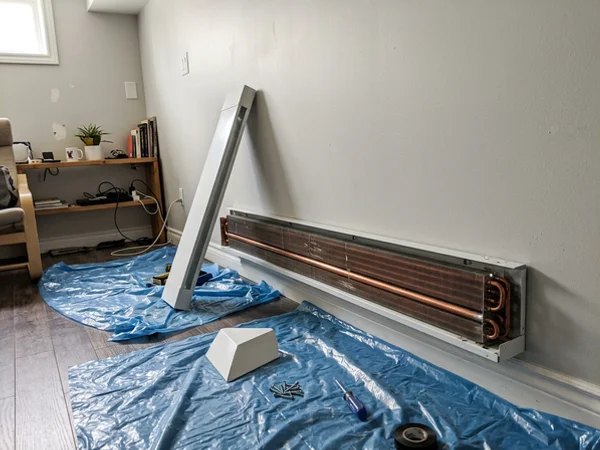 Hydronic baseboard convector being fitted along a basement wall