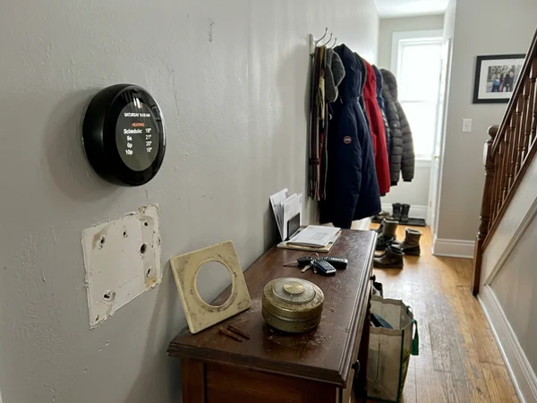 Smart thermostat mounted on a hallway wall beside the removed dial thermostat